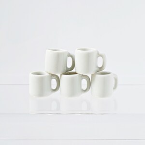 Bulk white ceramic miniature mugs piled together for quantity option display