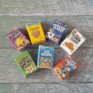 May include: A collection of eight miniature cereal boxes, including Raisin Bran, Cheerios, Frosted Flakes, Corn Flakes, Rice Krispies, Apple Jacks, and Cap'n Crunch. The boxes are arranged on a wooden surface.