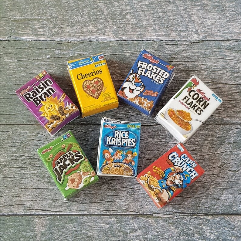 May include: A collection of eight miniature cereal boxes, including Raisin Bran, Cheerios, Frosted Flakes, Corn Flakes, Rice Krispies, Apple Jacks, and Cap'n Crunch. The boxes are arranged on a wooden surface.
