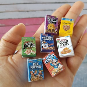 May include: A collection of miniature cereal boxes, including Raisin Bran, Cheerios, Frosted Flakes, Apple Jacks, Corn Flakes, Rice Krispies, and Cap'n Crunch. The boxes are all different colors and have various cartoon characters on them.