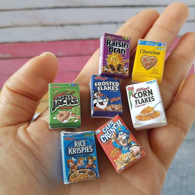 May include: A collection of miniature cereal boxes, including Raisin Bran, Cheerios, Frosted Flakes, Apple Jacks, Corn Flakes, Rice Krispies, and Cap'n Crunch. The boxes are all different colors and have various cartoon characters on them.