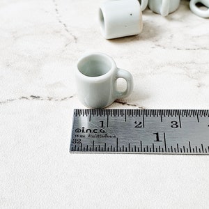 White miniature ceramic mug next to ruler showing 1.5 cm size scale