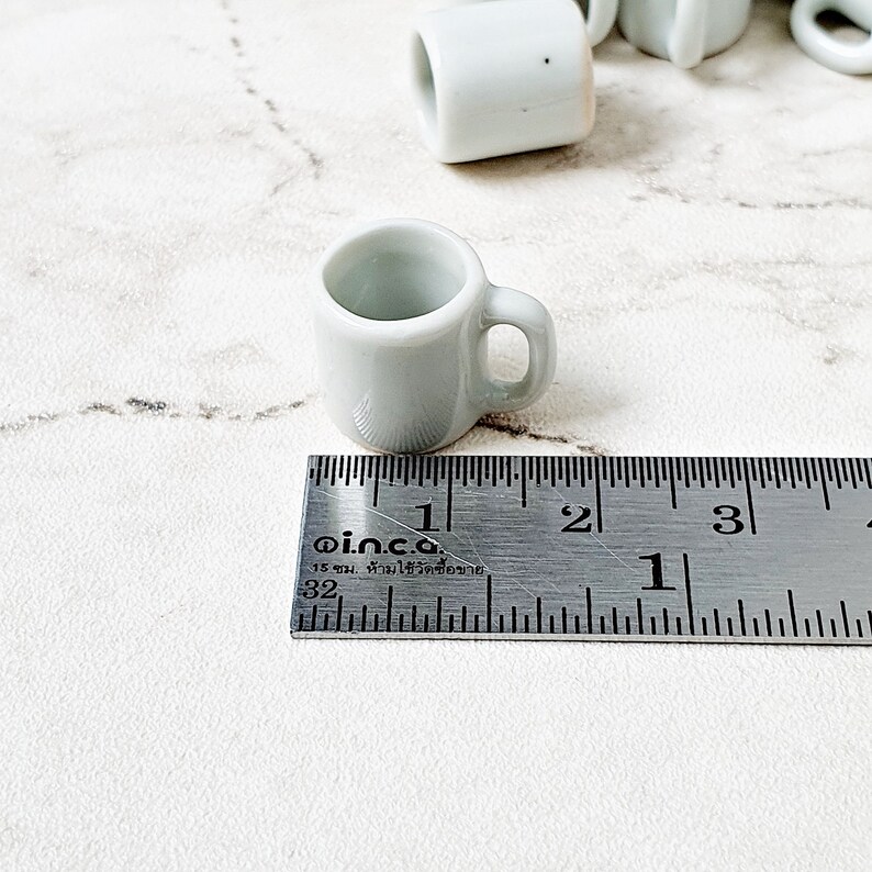 White miniature ceramic mug next to ruler showing 1.5 cm size scale