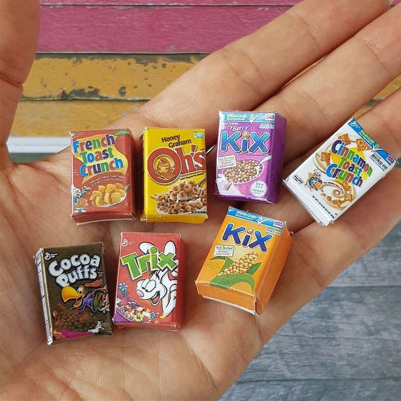 May include: A collection of miniature cereal boxes, including Cocoa Puffs, Trix, French Toast Crunch, Honey Graham Oh's, Cinnamon Toast Crunch, and two boxes of Kix.