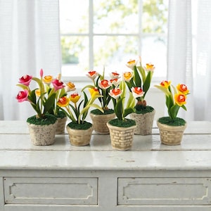 May include: A collection of miniature ceramic flower pots, each containing colorful artificial flowers. The flowers feature red, pink, yellow, and white petals with green leaves. The pots are beige and sit on a white surface.
