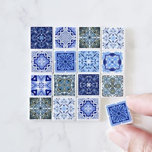 Op de afbeelding: Een set van 12 blauwe en witte keramische tegels met ingewikkelde bloem- en geometrische patronen. De tegels zijn vierkant en hebben een glanzende afwerking.
