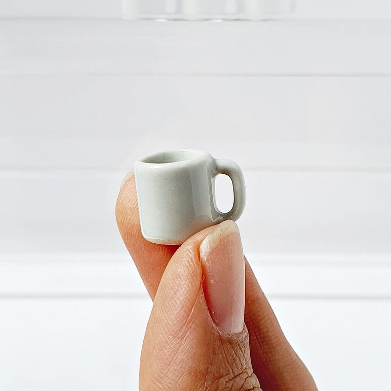 Single white ceramic miniature mug held between fingers, smooth glazed finish