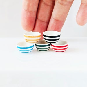 May include: Five miniature ceramic bowls with striped patterns in blue, green, red, black, and yellow. The bowls are stacked on top of each other.