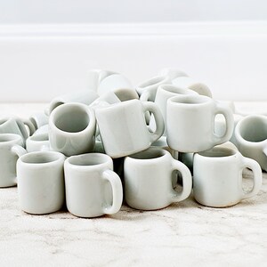 Multiple white miniature ceramic mugs grouped together on clean background