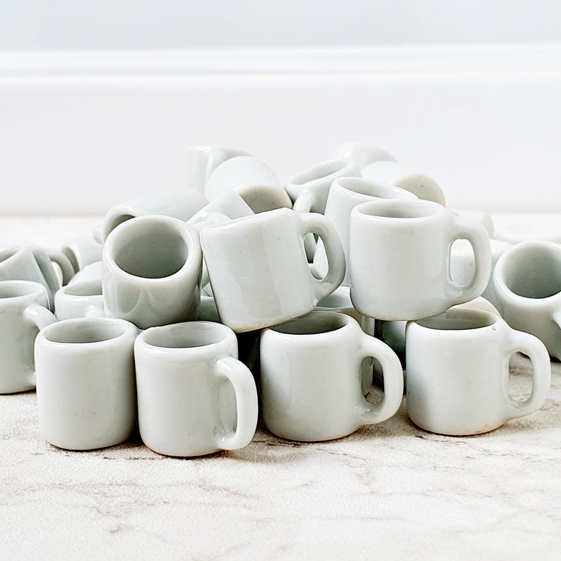 Multiple white miniature ceramic mugs grouped together on clean background