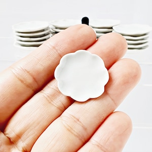 May include: A small, white ceramic plate with a scalloped edge. The plate is held in a hand.