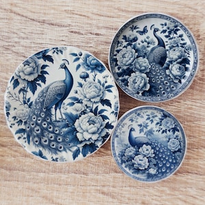 May include: Three blue and white porcelain plates with a peacock design. The plates feature a peacock with its tail feathers spread out, surrounded by flowers. The plates are perfect for adding a touch of elegance to any table setting.