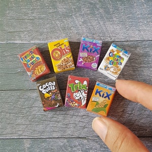 May include: A collection of miniature cereal boxes, including Honey Graham Oh's, Berry Berry Kix, Cinnamon Toast Crunch, Cocoa Puffs, Trix, and Kix. The boxes are all brightly colored and feature cartoon characters.