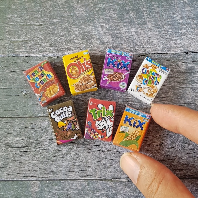 May include: A collection of miniature cereal boxes, including Honey Graham Oh's, Berry Berry Kix, Cinnamon Toast Crunch, Cocoa Puffs, Trix, and Kix. The boxes are all brightly colored and feature cartoon characters.