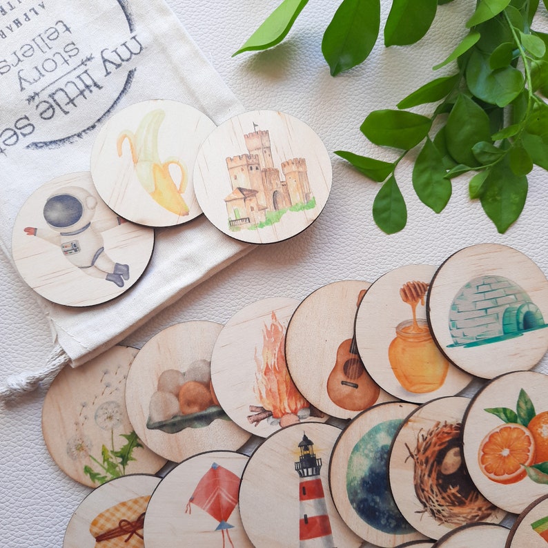 Puede incluir: Un conjunto de discos de madera para contar historias con ilustraciones de acuarela. Las ilustraciones incluyen un pl&aacute;tano, un castillo, un astronauta, una fogata, una guitarra, un panal de miel, un igl&uacute;, un diente de le&oacute;n, un nido, una naranja, una cometa, un faro, un planeta, una cesta y una pila de piedras.