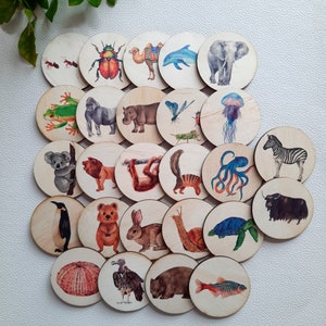 May include: A set of 20 wooden circle puzzle pieces featuring various animal and insect illustrations. The pieces are painted in bright colours and feature a variety of animals, including a camel, a penguin, a koala, a butterfly, a ladybug, a jellyfish, and an octopus.