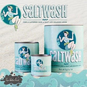 May include: Three different sized cans of blue and white paint with a vintage-style illustration of a woman painting on each can. The cans are labeled "Saltwash" and say "For a layered sun & salt air soaked look" and "Made with real sea salt".