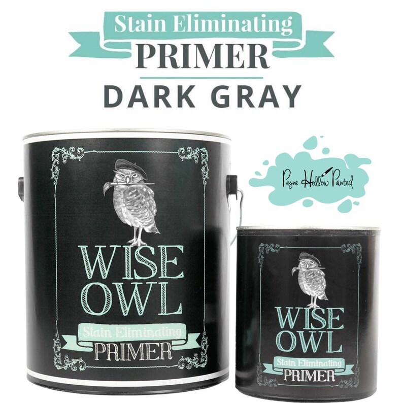 May include: Two dark gray paint cans with the text "WISE OWL Stain Eliminating PRIMER." The cans feature an illustration of an owl wearing a hat. The text "Stain Eliminating PRIMER DARK GRAY" is at the top.