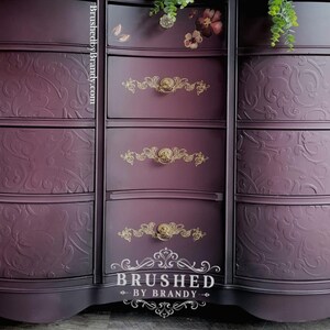 May include: A dark purple chest of drawers with gold handles and embossed floral patterns. The chest has multiple drawers and a curved design. The text "Brushed by Brandy" is visible at the bottom.