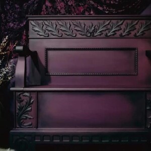 May include: A dark purple bench with ornate leaf carvings. The bench features a rectangular panel and decorative trim. The overall design is gothic and elegant, with a focus on detailed craftsmanship and a vintage aesthetic.