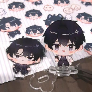 May include: Two black and white anime character acrylic stands. The characters are wearing different outfits and have different expressions. The stands are on a clear acrylic base.