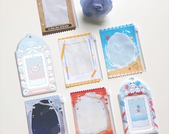 May include: A collection of decorative card holders with various designs. The holders feature themes like a wanted poster, a beach scene, and a starry night. Each holder has a clear window for displaying cards or photos.