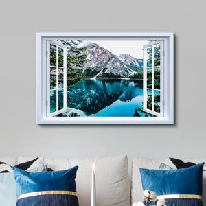 May include: A white framed canvas print of a window view of a lake and mountains. The lake is a bright blue and the mountains are snow-capped. The window is open and the view is framed by green trees.