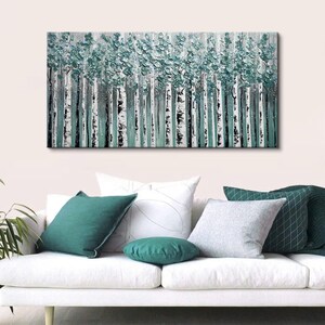 Op de afbeelding: Abstract schilderij van een bos met witte berkenstammen en turquoise groen gebladerte. Het kunstwerk hangt boven een witte bank met turquoise en grijze kussens.