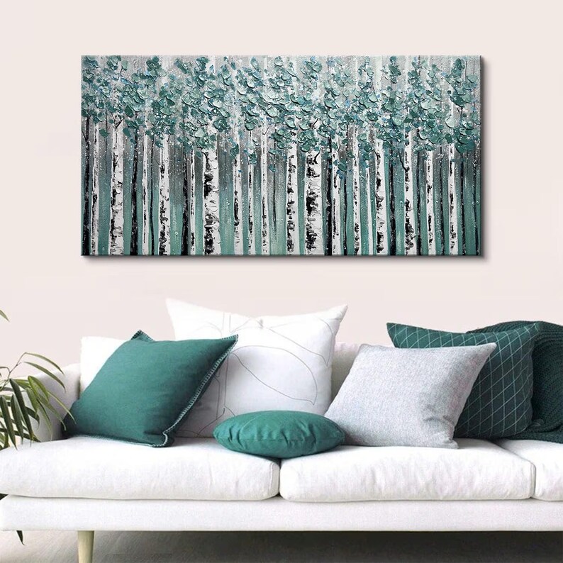Op de afbeelding: Abstract schilderij van een bos met witte berkenstammen en turquoise groen gebladerte. Het kunstwerk hangt boven een witte bank met turquoise en grijze kussens.