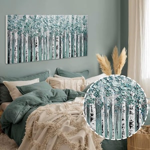 Op de afbeelding: Een rechthoekig canvas kunstwerk met een berkenbos. Het kunstwerk maakt gebruik van getextureerde turquoise en witte verf, met zwart-witte boomstammen. Het kunstwerk hangt boven een bed met turquoise beddengoed en een cr&egrave;mekleurige sprei.