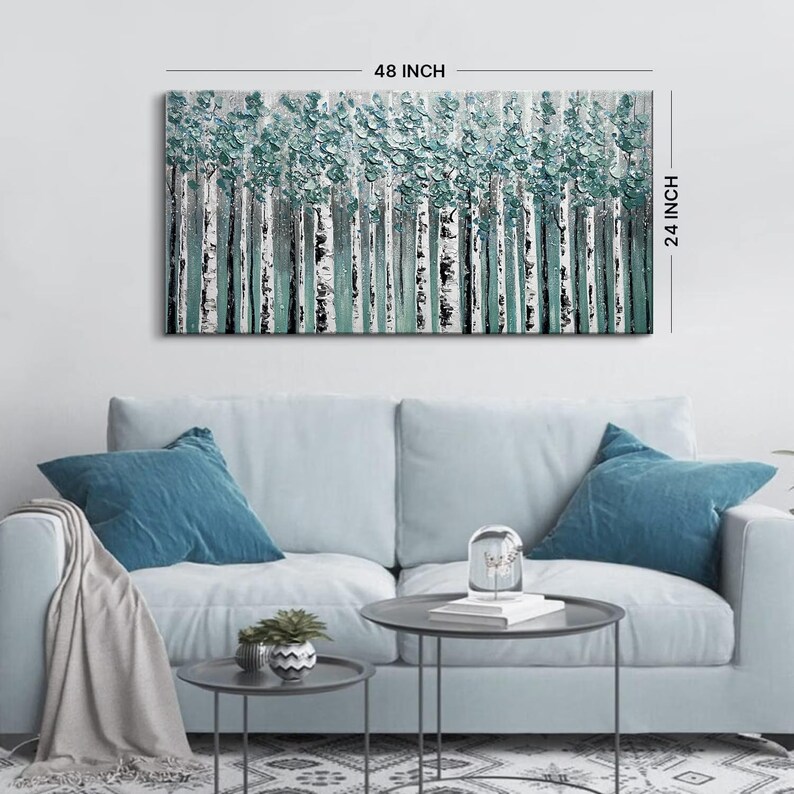 Op de afbeelding: Een rechthoekig canvas kunstwerk met een boslandschap. Het kunstwerk is 122 cm breed en 61 cm hoog. De bomen hebben witte stammen met zwarte markeringen en blauwgroen blad. Het schilderij hangt boven een lichtblauwe bank.