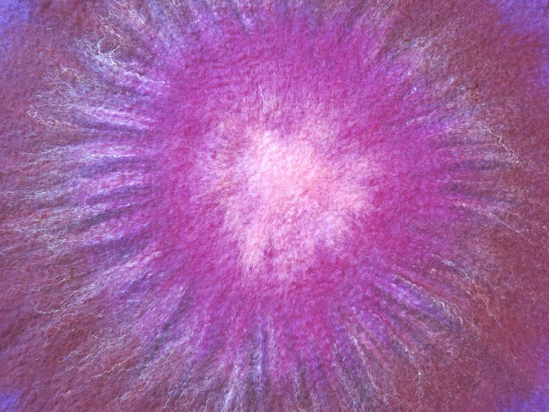 Puede incluir: Una superficie de lana fieltrada texturizada con un patr&oacute;n radial vibrante. El centro es de un rosa p&aacute;lido brillante que transiciona a tonos magenta intenso y morado oscuro, con fibras blancas finas que irradian hacia el exterior.