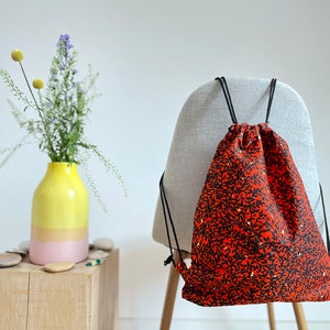 May include: A red drawstring bag with a black floral pattern. The bag is hanging on the back of a chair.