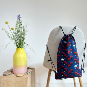 May include: A blue drawstring bag with a red and white mushroom pattern. The bag is hanging on the back of a chair.