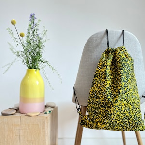 May include: A yellow and green drawstring bag with a black drawstring. The bag is hanging on the back of a chair.
