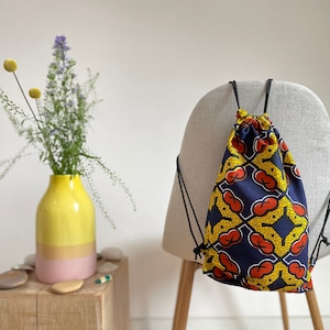 May include: A blue drawstring bag with a yellow and red geometric pattern. The bag is hanging on a chair.