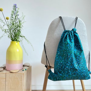 May include: A blue drawstring bag with a white and green floral pattern. The bag is hanging on the back of a chair.