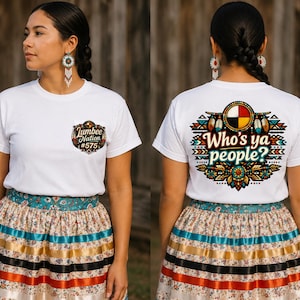 Puede incluir: Una camiseta blanca de manga corta con un pequeño logotipo de Lumbee Nation #575 en el pecho izquierdo y un gráfico grande y colorido en la espalda con el texto Who's ya people? rodeado de patrones geométricos, plumas y una rueda medicinal.