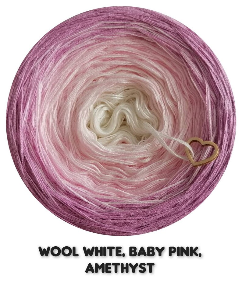 Op de afbeelding: Een ronde bol garen in een kleurengradatie, waaronder wit, babyroze en amethist. Een houten hartvormige bedel is aan het garen bevestigd. De tekst "WOOL WHITE, BABY PINK, AMETHYST" staat onderaan.