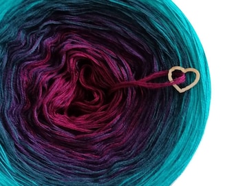 May include: A vibrant ball of yarn in teal, purple, and magenta, with a wooden heart-shaped charm. The yarn's colours blend from teal to purple to magenta. Suitable for knitting and crochet.