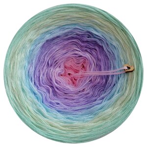 May include: A ball of yarn with a gradient of colors from green to blue to purple to pink. The yarn is wound into a circle and has a wooden tag attached to it.