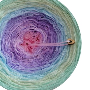 May include: A skein of ombre yarn in shades of green, blue, purple, and pink. The yarn is wound into a circle and has a wooden heart-shaped tag attached.