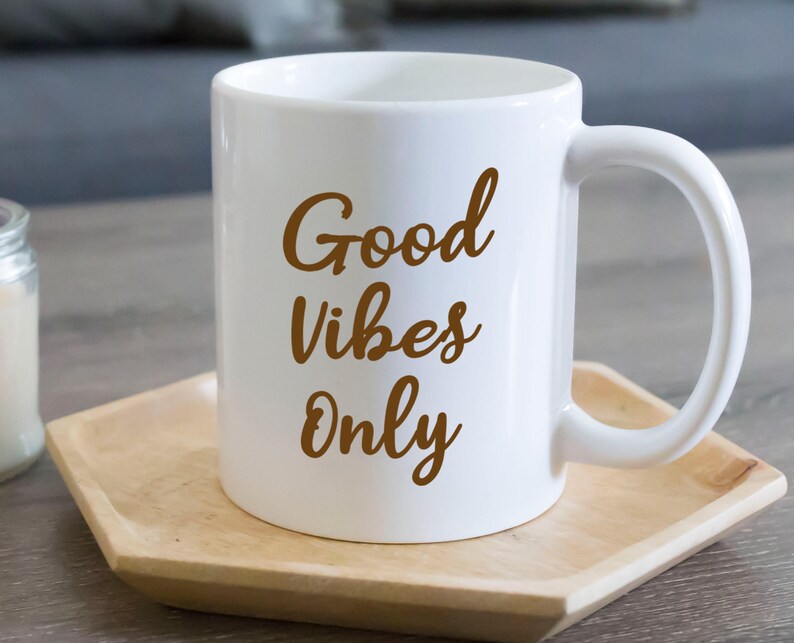 May include: White ceramic mug with the words "Good Vibes Only" in a brown script. The mug sits on a light brown wooden tray. The mug has a curved handle.