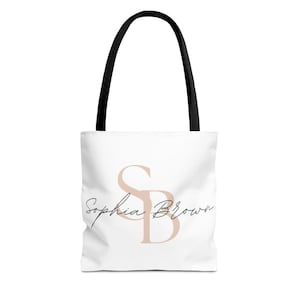 May include: White tote bag with black handles featuring the name "Sophia Brown" in a cursive font, with the initials "SB" in a light brown color. The bag is designed for carrying items.