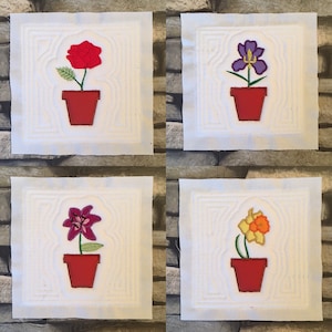 May include: Four white square fabric panels with embroidered images of flowers in pots. The flowers are a red rose, a purple iris, a pink lily, and a yellow daffodil.