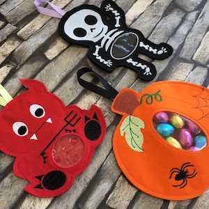 May include: Three Halloween treat bags, one shaped like a pumpkin, one like a devil, and one like a skeleton. The bags are made of felt and have embroidered details. The pumpkin bag has a clear window to see the sweets inside.