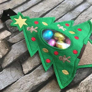 May include: Green felt Christmas tree-shaped gift bag with a clear plastic window, filled with wrapped chocolate candies. The bag has a brown felt base and a black hanging loop.
