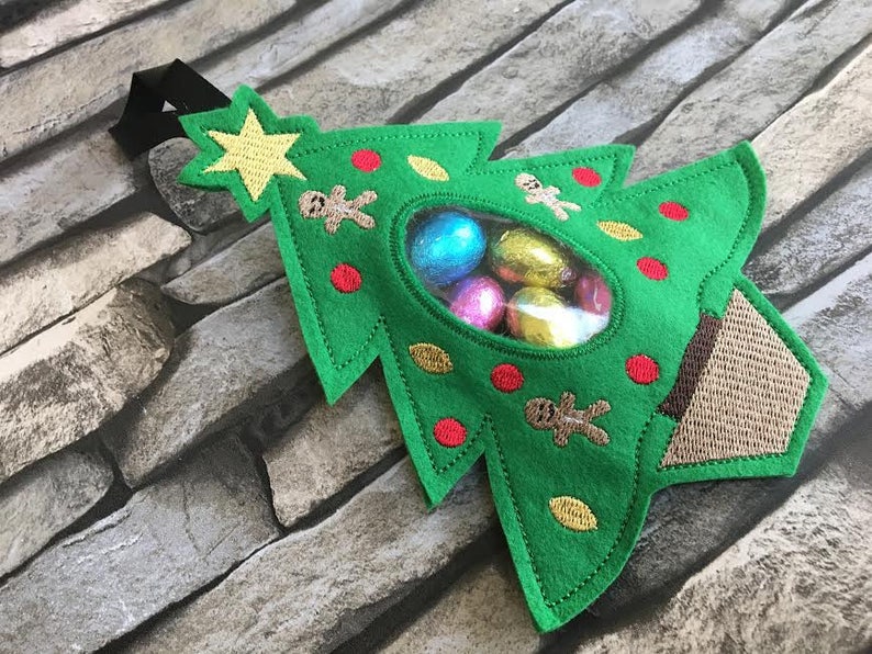 May include: Green felt Christmas tree-shaped gift bag with a clear plastic window, filled with wrapped chocolate candies. The bag has a brown felt base and a black hanging loop.