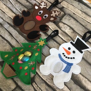 May include: Three felt Christmas ornaments, a reindeer, a Christmas tree, and a snowman. Each ornament has a clear plastic window for holding small treats or candy.