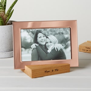 May include: A rose gold picture frame with a black and white photo, resting on a wooden stand. The stand is engraved with "Mum & Me". Another wooden stand is engraved with "Thanks mom for everything. Love you so much and always xxx."